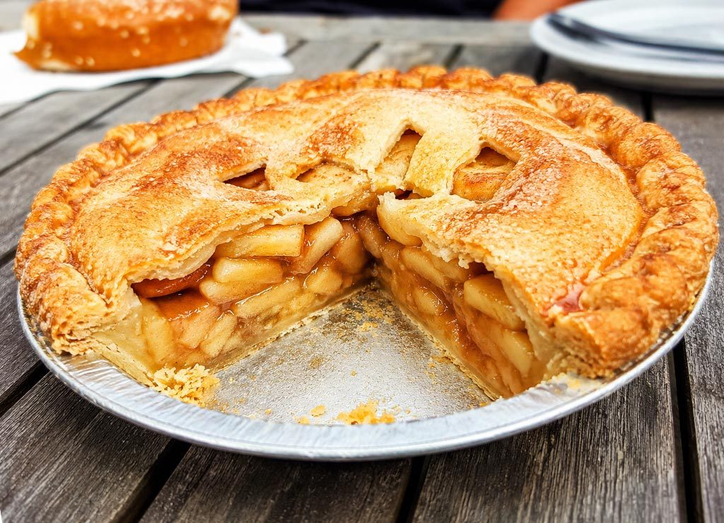 National Apple Pie Day – Tag des Apfelkuchens in den USA. Kuriose Feiertage - 13. Mai © 2026 Sven Giese – Bild 1 Angeschnittener Apple Pie mit goldbrauner Kruste auf rustikalem Holztisch.