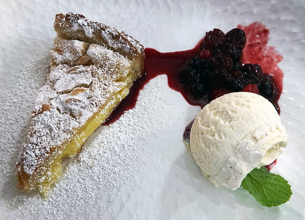 National Vanilla Ice Cream Day – Vanilleeis-Tag in den USA. Kuriose Feiertage – 23. Juli © 2026 Sven Giese – Bild 3 Apfelkuchen mit Puderzucker, Vanilleeis, Beerenkompott und Minze auf einem weißen Teller angerichtet.