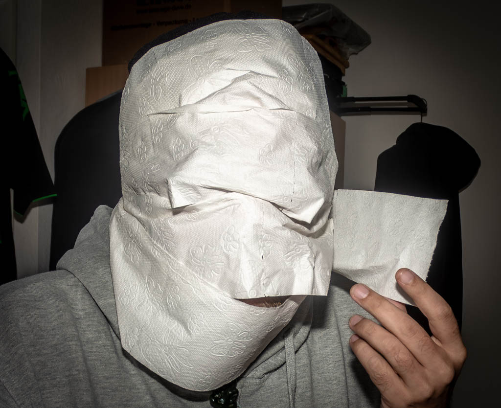 National Toilet Paper Day – Tag des Toilettenpapiers in den USA. Kuriose Feiertage - 26. August © 2024 Sven Giese – Bild 4 Eine Person, die ihr Gesicht vollständig mit Toilettenpapier bedeckt hat, hält ein zusätzliches Stück Toilettenpapier in der Hand.