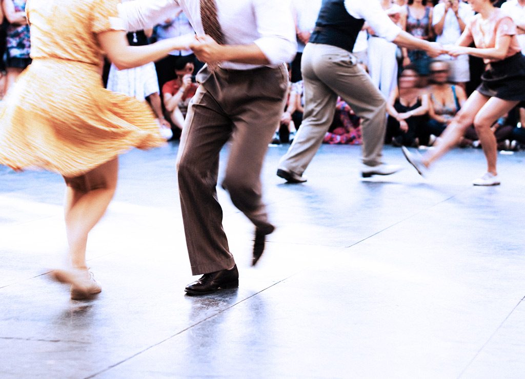 Mehrere Lindy-Hop-Paare tanzen draußen, Bewegungsunschärfe zeigt schnelle Schritte.