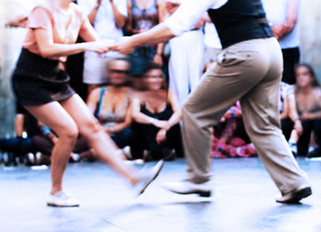Lindy-Hop-Paar tanzt eng gefasst mit Bewegungsunschärfe vor Zuschauern im Hintergrund.