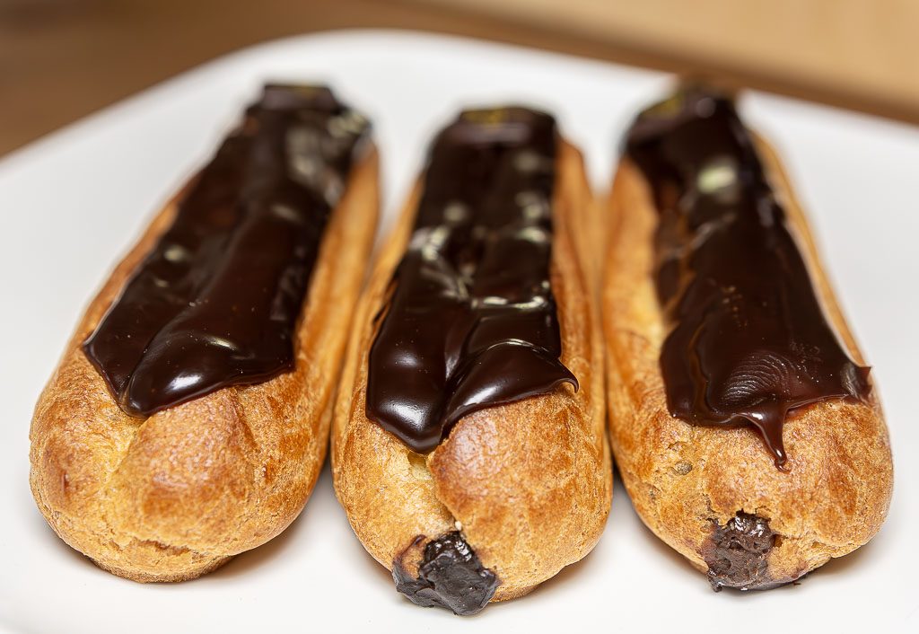 Drei goldbraune Éclairs mit glänzendem Schokoladenguss liegen nebeneinander auf Teller.