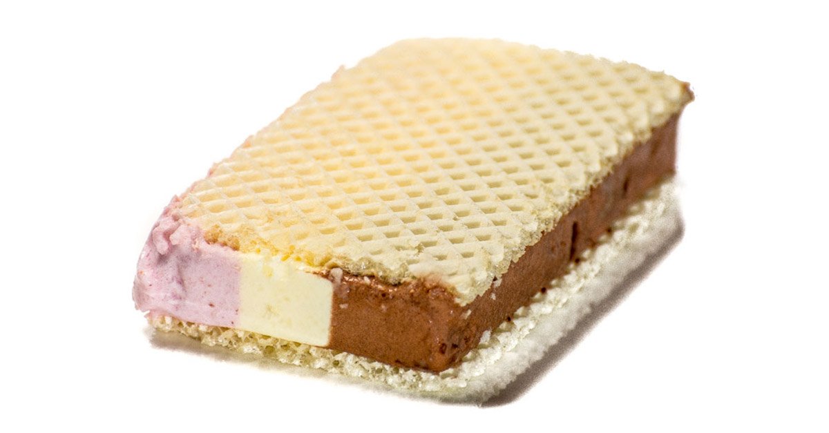 Ein Sandwich-Eis mit Erdbeere, Vanille und Schokoladeneis zwischen zwei Waffeln, leicht seitlich fotografiert auf weißem Hintergrund. 