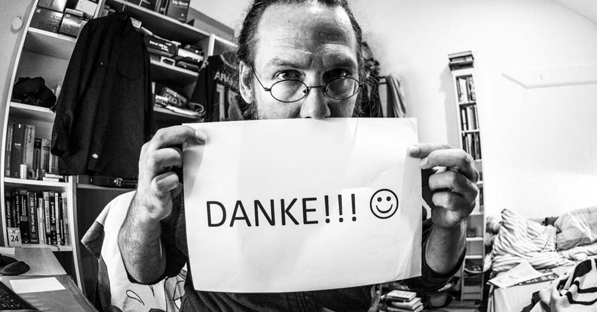 Schwarz-Weiß-Foto von einer Person, die ein Schild mit der Aufschrift „DANKE!!!“ und einem Smiley hochhält.