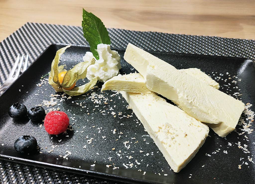 Scheiben von Parfait auf schwarzem Teller, mit Physalis, Beeren, Sahnetupf und Minzblatt garniert.