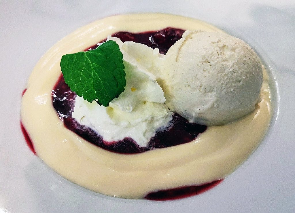 Vanilleeis mit heller Sauce und roter Beerenkompott, Sahnehäubchen und frischem Minzblatt obenauf.