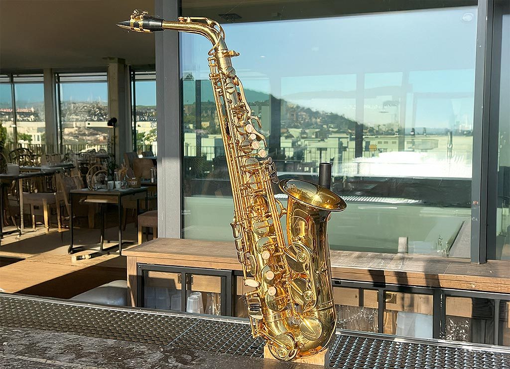 Ein glänzendes, goldenes Saxofon steht auf einer Bar, im Hintergrund Stadtblick.