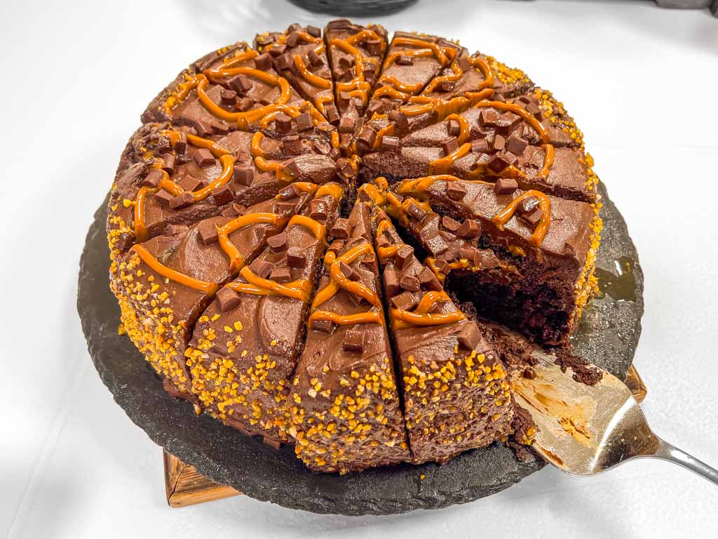 Schokoladenkuchen mit Karamellverzierung und Kuchenheber, ein Stück bereits entnommen.
