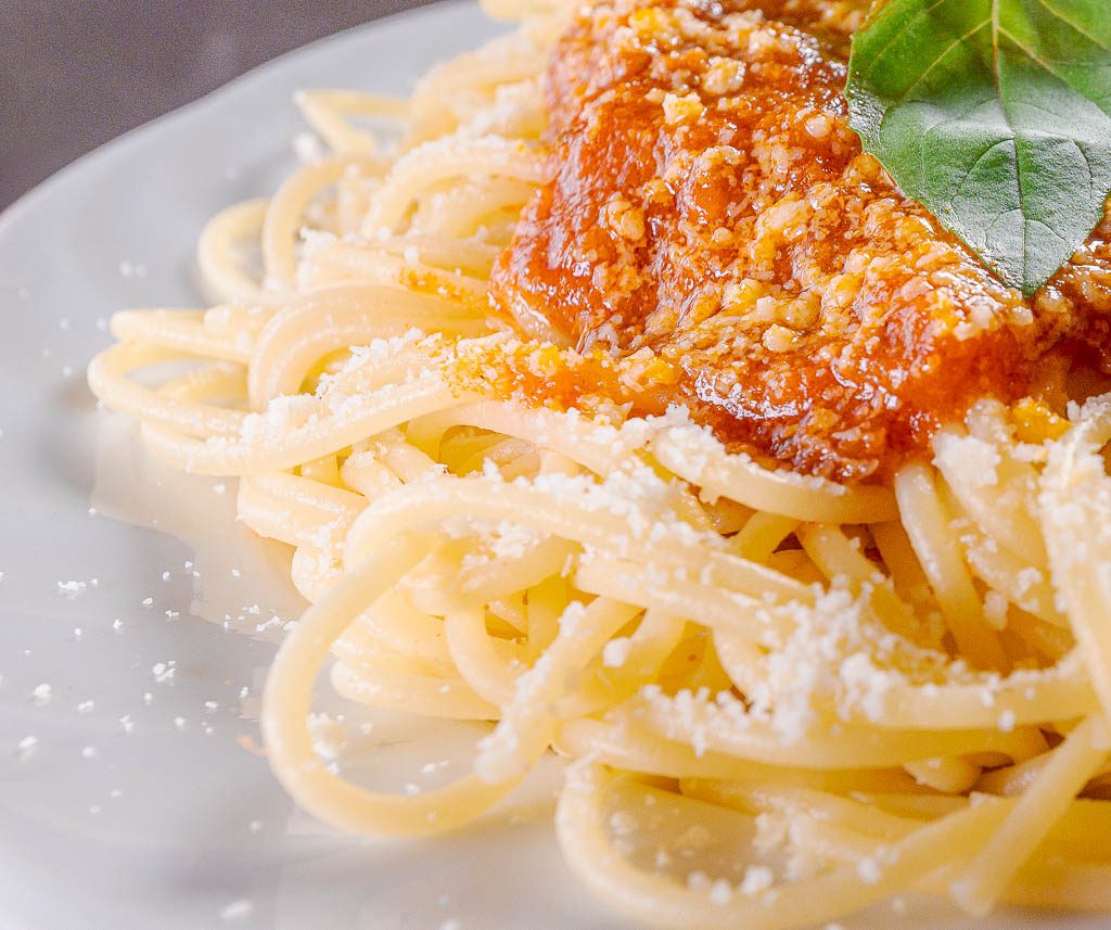 Spaghettiteller mit Tomatensauce, geriebenem Käse und frischem Basilikumblatt auf weißem Teller.