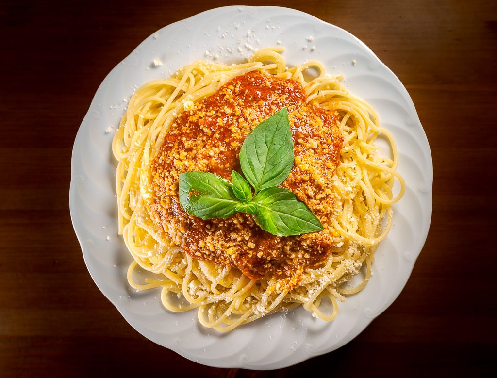 Spaghettiteller von oben mit Tomatensauce, Basilikum und Parmesan auf weißem Teller serviert.