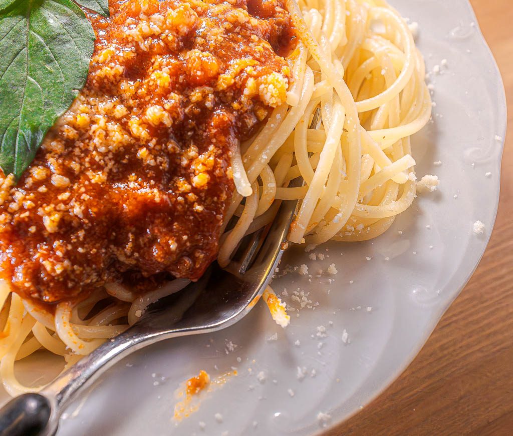 Nahaufnahme von Spaghetti mit Tomatensauce und Parmesan, Gabel schiebt sich in die Nudeln.