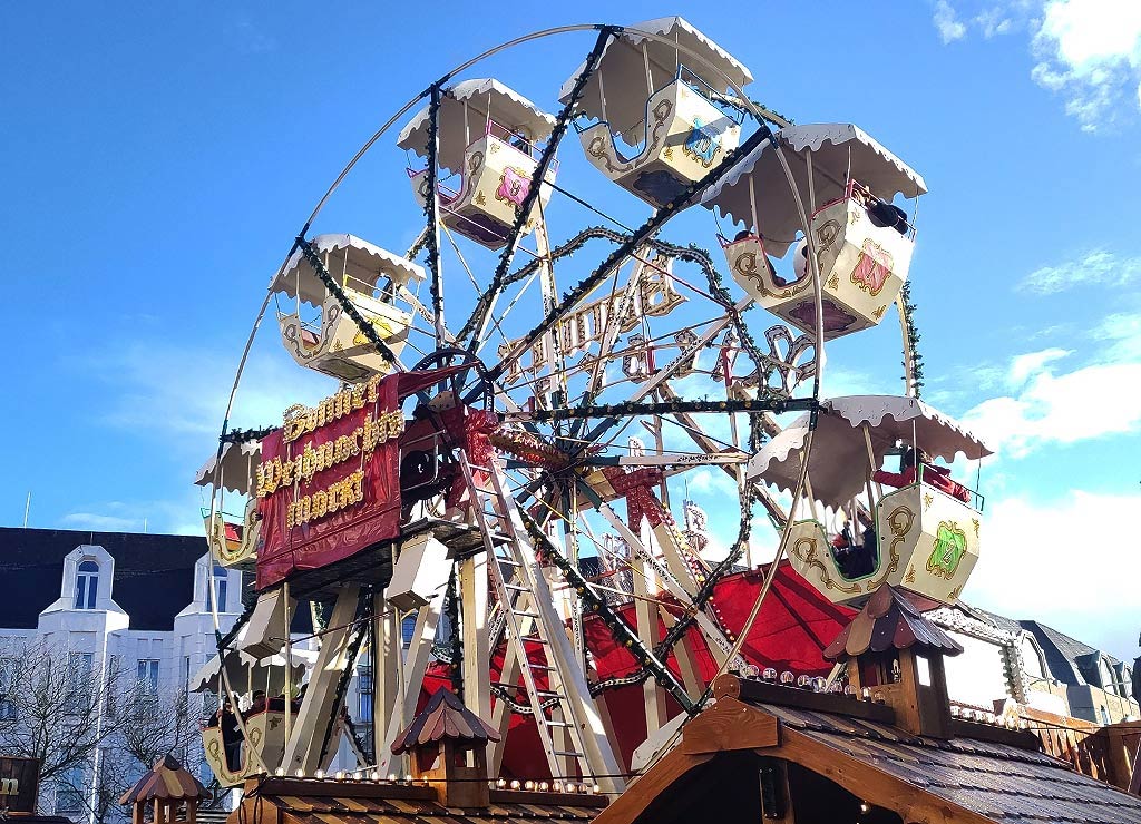 Ein kleines, dekoriertes Riesenrad mit roten und weißen Gondeln auf einem Weihnachtsmarkt.