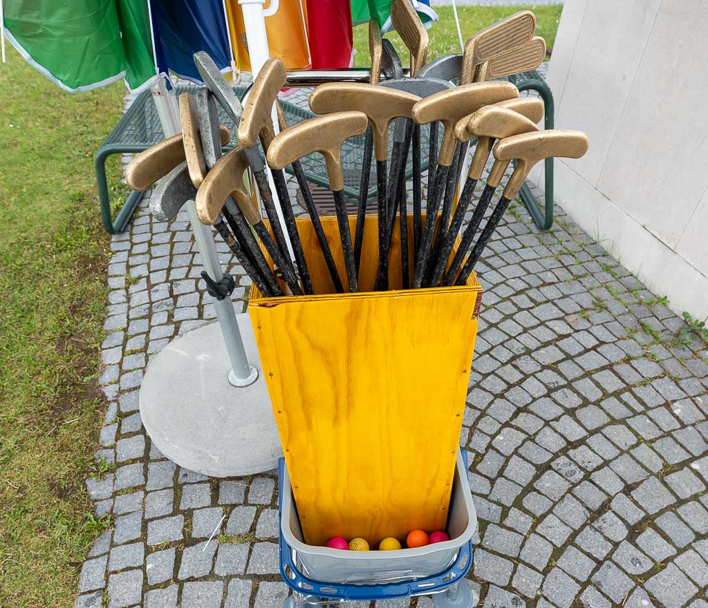National Miniature Golf Day – Nationaler Minigolf-Tag in den USA. Kuriose Feiertage – zweiter Samstag im Mai © 2026 Sven Giese - Bild 2 Mehrere Minigolfschläger stecken in gelber Kiste, bunte Bälle liegen unten bereit.