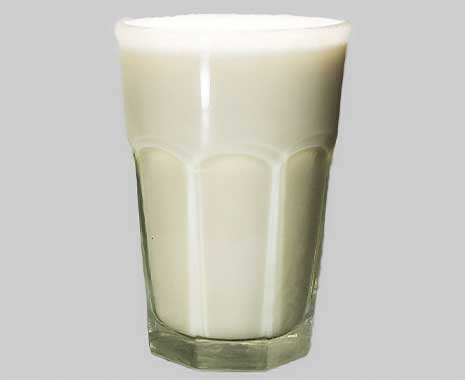 Glas mit Vanille-Milchshake auf grauem Hintergrund, Bläschen oben sichtbar.