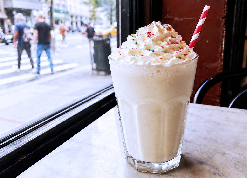 Vanille-Milchshake mit Sahne, Streuseln und Strohhalm am Caféfenster in New York