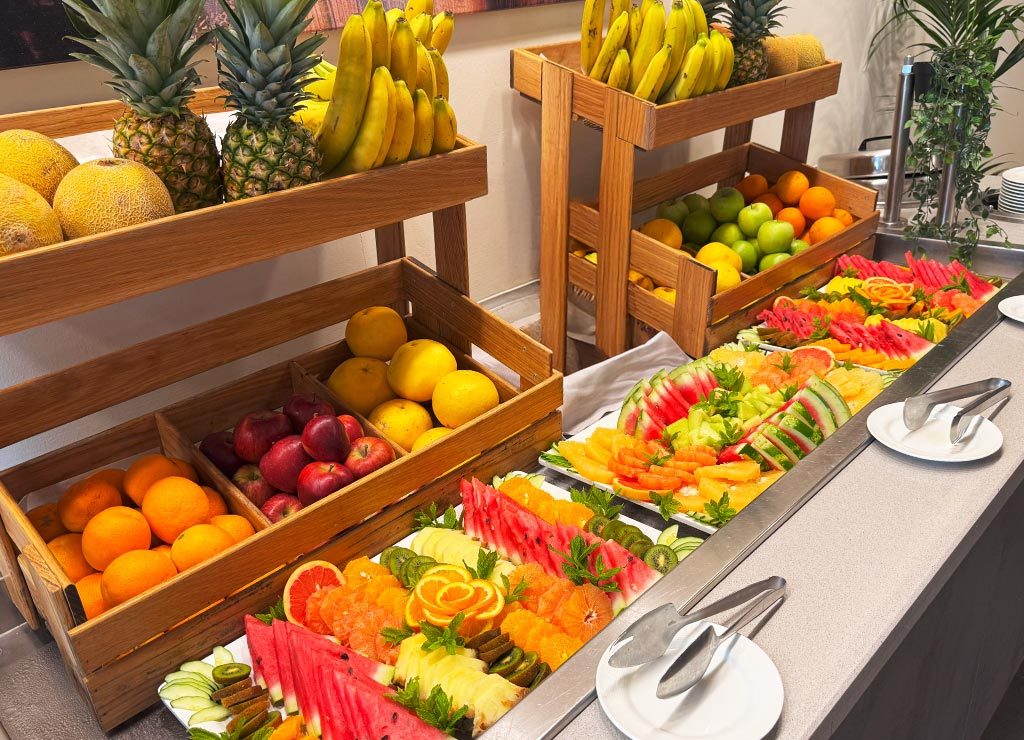 Reich gedecktes Obstbuffet mit geschnittenen Melonen, Orangen, Kiwis und ganzen Früchten.