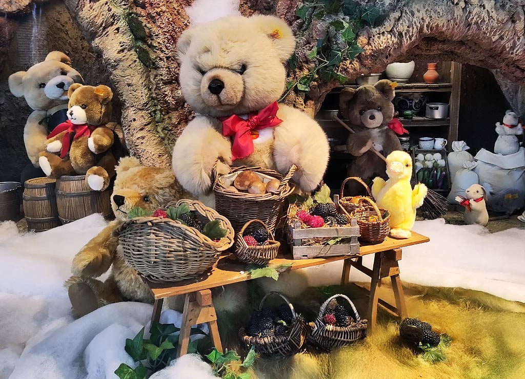 Teddy Bear Picnic Day – Tag des Teddybär-Picknick. Kuriose Feiertage - 10. Juli © 2025 Sven Giese – Bild 2 Teddybären und Stofftiere feiern vor einem Baumstamm mit Körben voller Obst.
