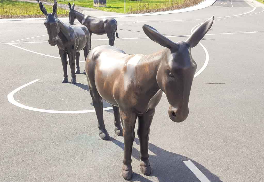 National Mule Appreciation Day - Ehrentag des Maultiers oder Muli-Tag in den USA. Kuriose Feiertage - 26. Oktober © 2018 Sven Giese - Bild 2 Drei bronze-schwarze Eselskulpturen stehen hintereinander auf einem asphaltierten Platz mit weißen Markierungen.