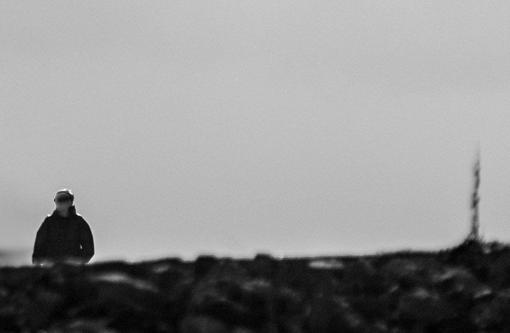Schwarz-weißes Bild einer einsamen Person in dunkler Kleidung, die in einer weiten, leeren Landschaft steht.