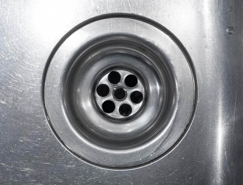 Nahaufnahme eines sauberen Edelstahl-Spülbeckens mit kreisförmigem Abfluss in der Mitte.