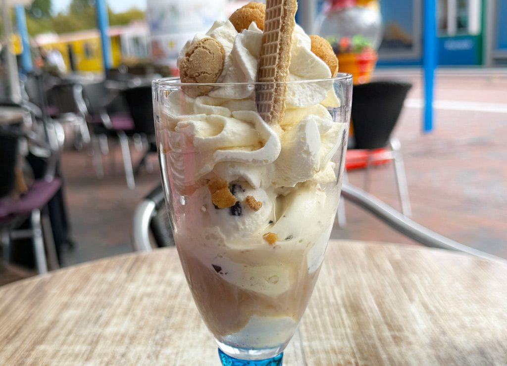 Großer Eisbecher mit Vanilleeis, Sahne, Keksen und Waffel auf Cafétisch draußen serviert.