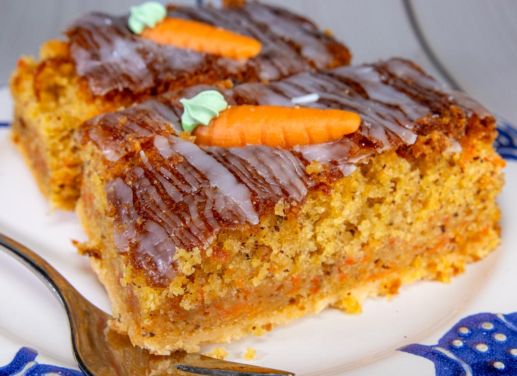 National Carrot Cake Day – Tag des Karottenkuchens in den USA. Kuriose Feiertage 3. Februar © 2024 Sven Giese - Bild 1 Zwei Stücke saftiger Karottenkuchen mit Zuckerguss und Marzipan-Möhren auf einem Teller.