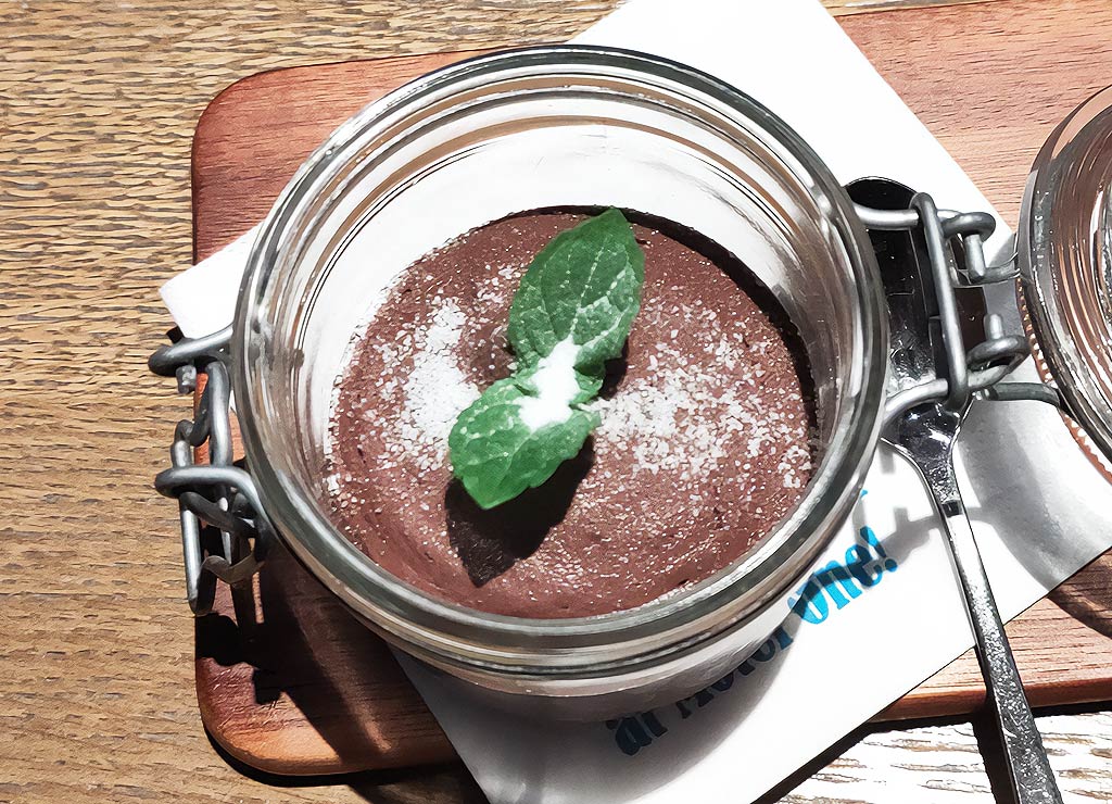 National Chocolate Mousse Day – Tag der Schokoladenmousse in den USA. Kuriose Feiertage - 3. April © 2024 Sven Giese – Bild 3 Glas mit Schokoladenmousse, Minzblatt und Puderzucker auf Holzbrett serviert.