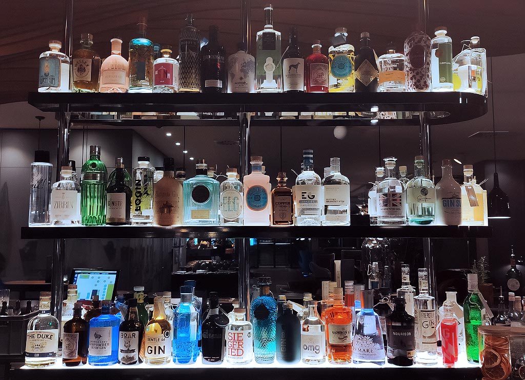 Welttag des Gin – World Gin Day. Kuriose Feiertage – zweiter Samstag im Juni © 2024 Sven Giese – Bild 2 Regal mit dutzenden Ginflaschen in unterschiedlichen Formen und Farben.