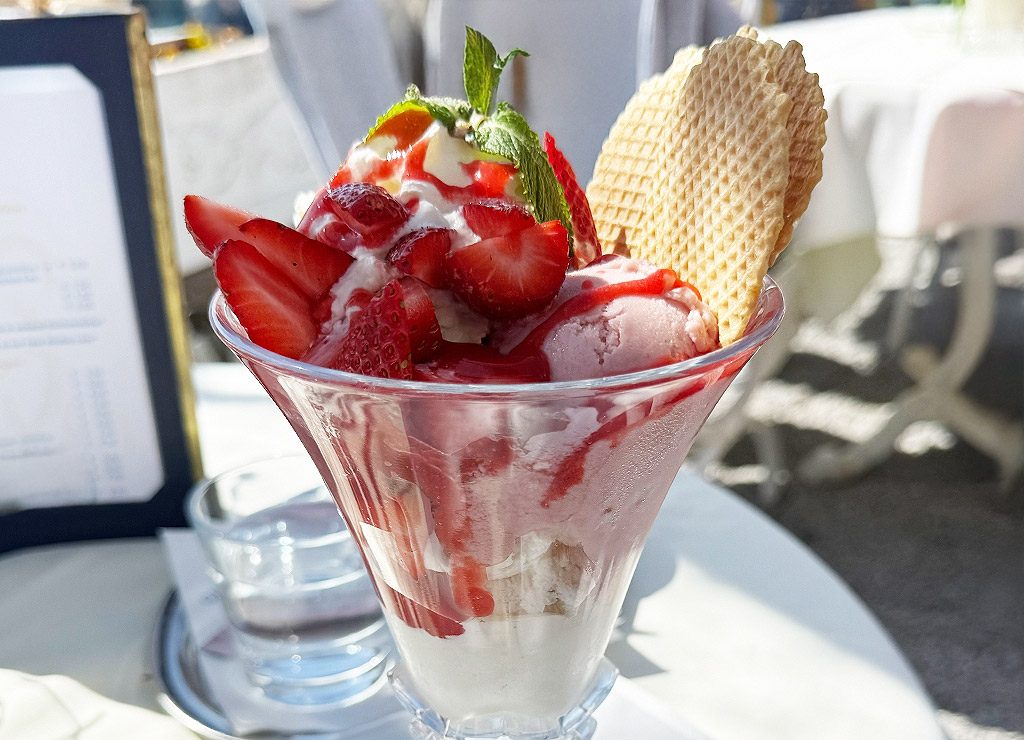 National Ice Cream Day – Tag des Eiscreme in den USA. Kuriose Feiertage – dritter Sonntag im Juli (c) 2025 Dietmar Giese – Bild 2 Erdbeer-Eisbecher mit frischen Erdbeeren, Sahne, Minze und Waffel auf Café-Tisch.