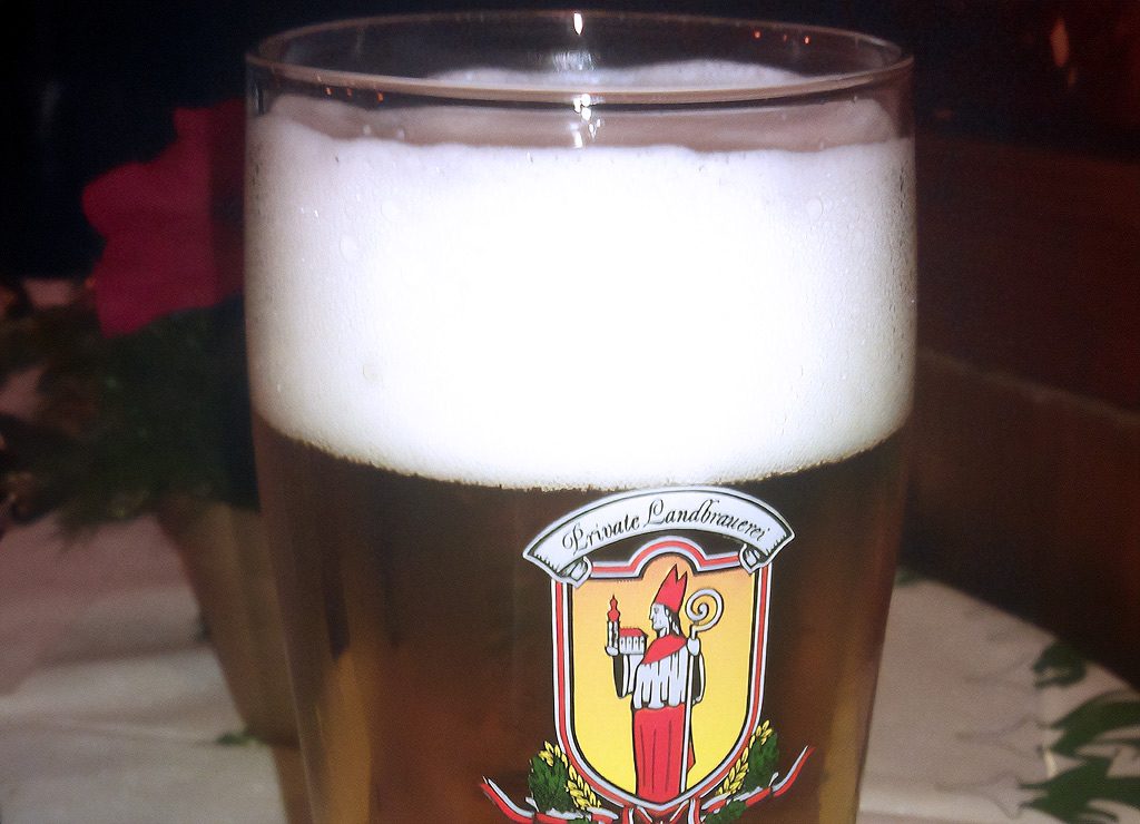 Ein Glas Bier mit Schaumkrone und dem Logo einer privaten Landbrauerei auf dem Glas.
