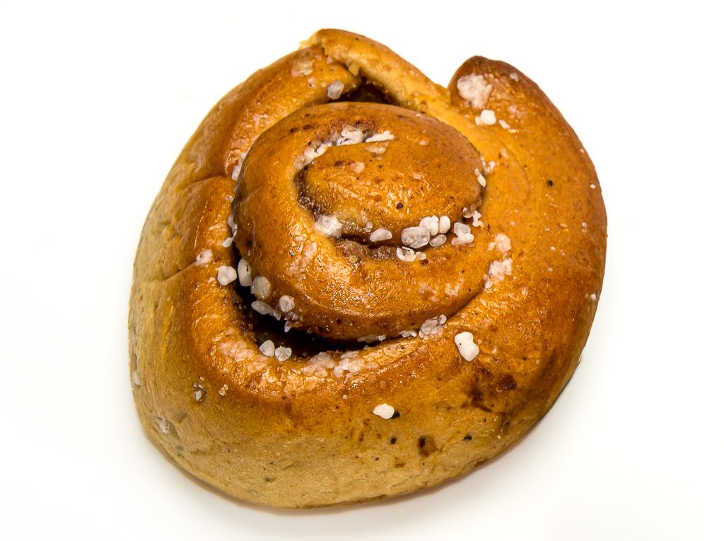 Einzelne goldbraune Zimtschnecke mit Hagelzucker vor schlichtem weißem Hintergrund.