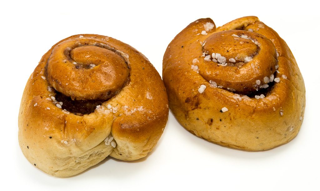 Zwei goldbraune schwedische Zimtschnecken mit Hagelzucker auf weißem Hintergrund.