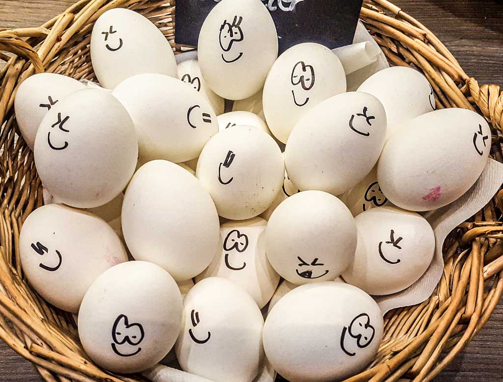 World Egg Day - der internationale Welt-Ei-Tag. Kuriose Feiertage - zweiter Freitag im Oktober © 2019 Sven Giese - Bild 1 Weiße Eier in einem Korb, auf die unterschiedliche fröhliche Gesichter gezeichnet sind.