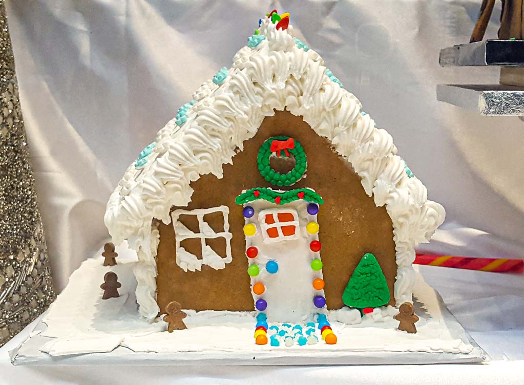 Lebkuchenhaus mit weißer Glasur, bunten Zuckerdekorationen und grünem Tannenbaum aus Zuckerguss.