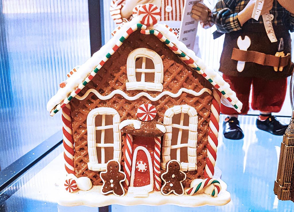 Lebkuchenhaus mit dekorativen Zuckerstangen und Pfefferminzdetails vor weihnachtlichem Hintergrund.