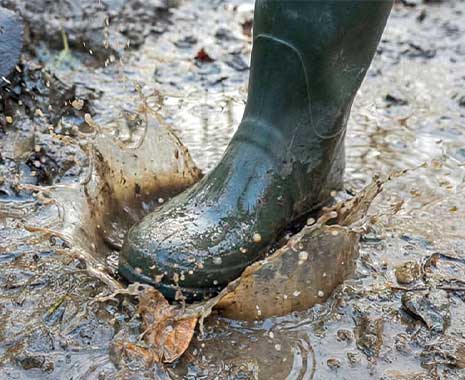 Gummistiefel tritt in schlammige Pfütze, Wasser und Matsch spritzen dynamisch nach oben.