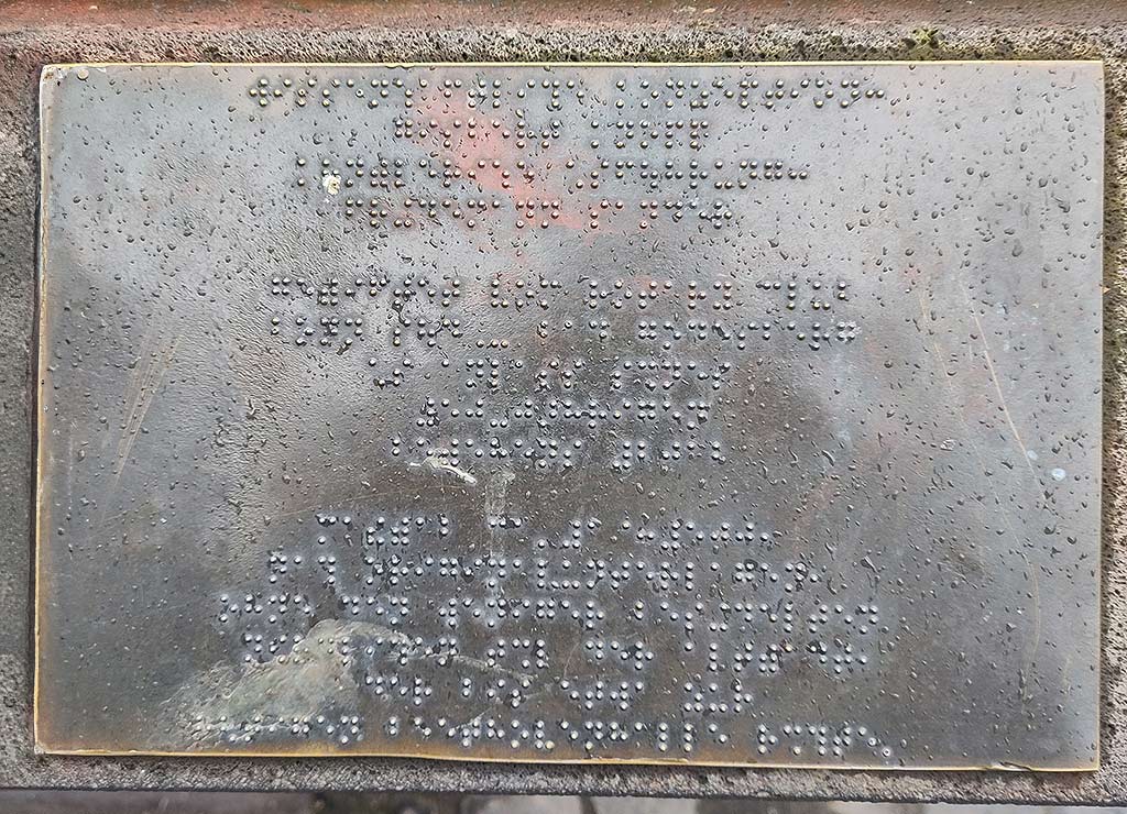 World Braille Day – der internationale Welt-Braille-Tag. Kuriose Feiertage - 4. Januar © 2024 Sven Giese. Messingtafel mit Blindenschrift, die bei Nässe glänzt und an einer Mauer angebracht ist.