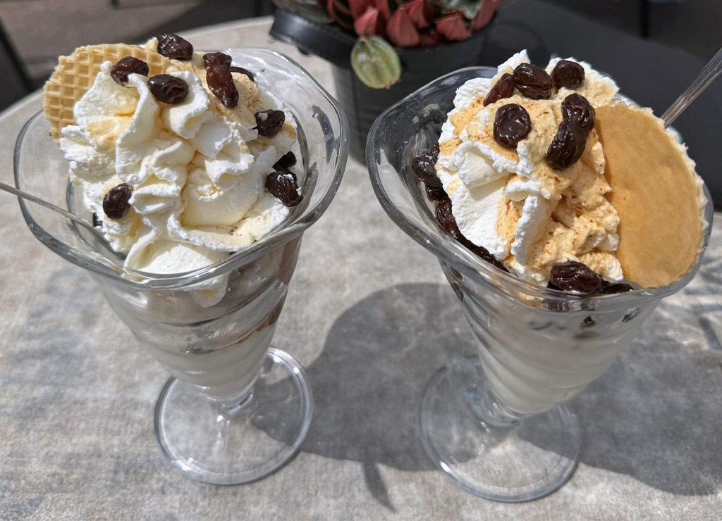 Zwei Eisbecher mit Sahne, Rosinen und Waffeln stehen nebeneinander auf einem Tisch.