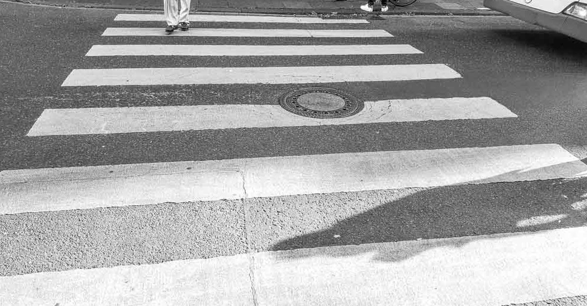 Tag des Zebrastreifens in Deutschland. Kuriose Feiertage - 1. September © 2023 Sven Giese – Bild 1 Ein schwarz-weißes Foto eines Zebrastreifens, auf dem eine Person in weißen Hosen die Straße überquert.