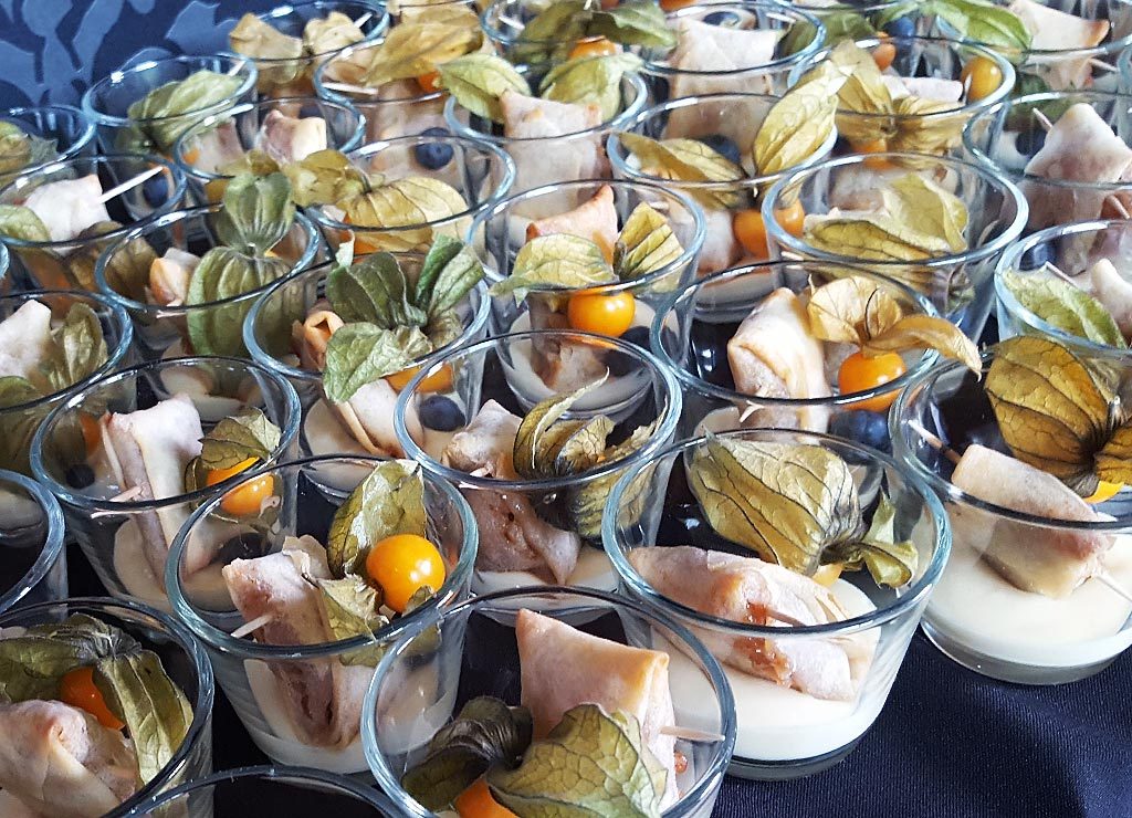 Mehrere Dessertgläser, die mit einer Mischung aus Blätterteiggebäck, Physalis-Früchten und einer Creme befüllt sind. Die Physalis-Früchte sind dabei prominent auf der Spitze platziert.