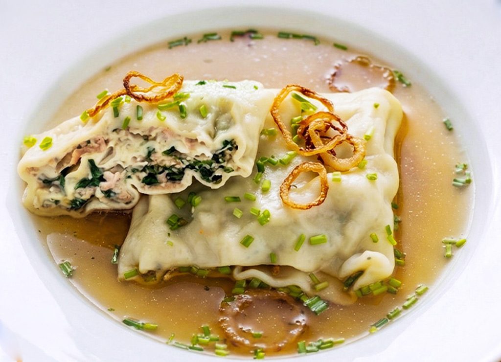 Weltmaultaschentag. Kuriose Feiertage – Gründonnerstag © 2026 Sven Giese - Bild 3 Maultaschen in Brühe mit Schnittlauch und Röstzwiebeln, eine Tasche aufgeschnitten, Füllung sichtbar.