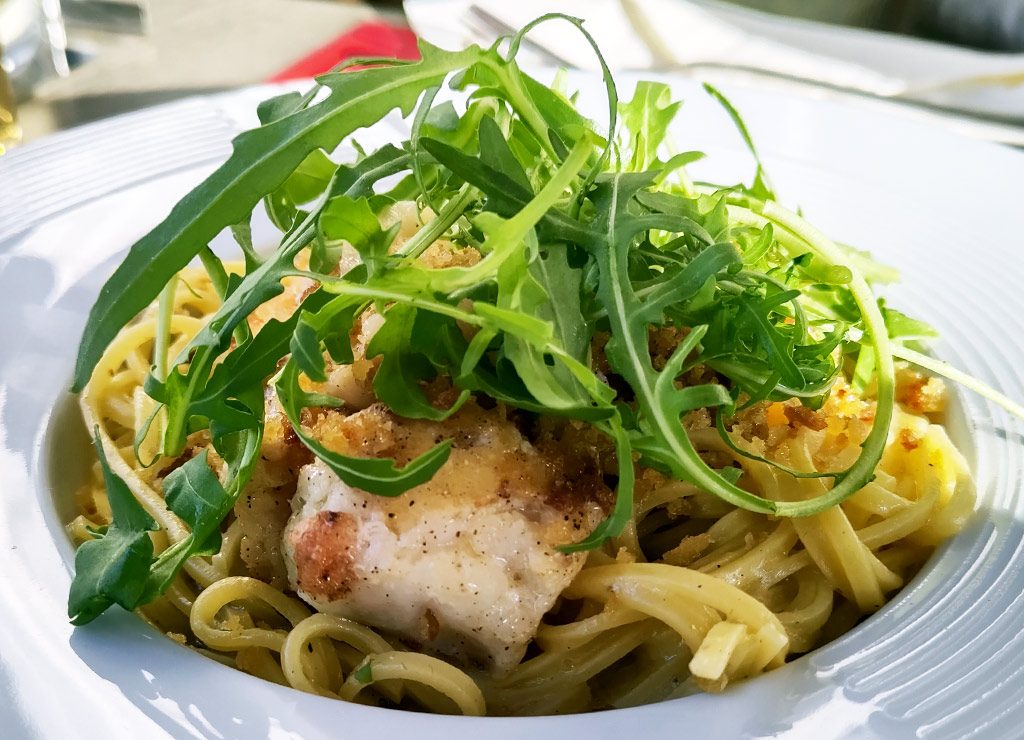 Teller Linguine mit gebratenem Fisch, goldbraunen Bröseln und frischem Rucola serviert.