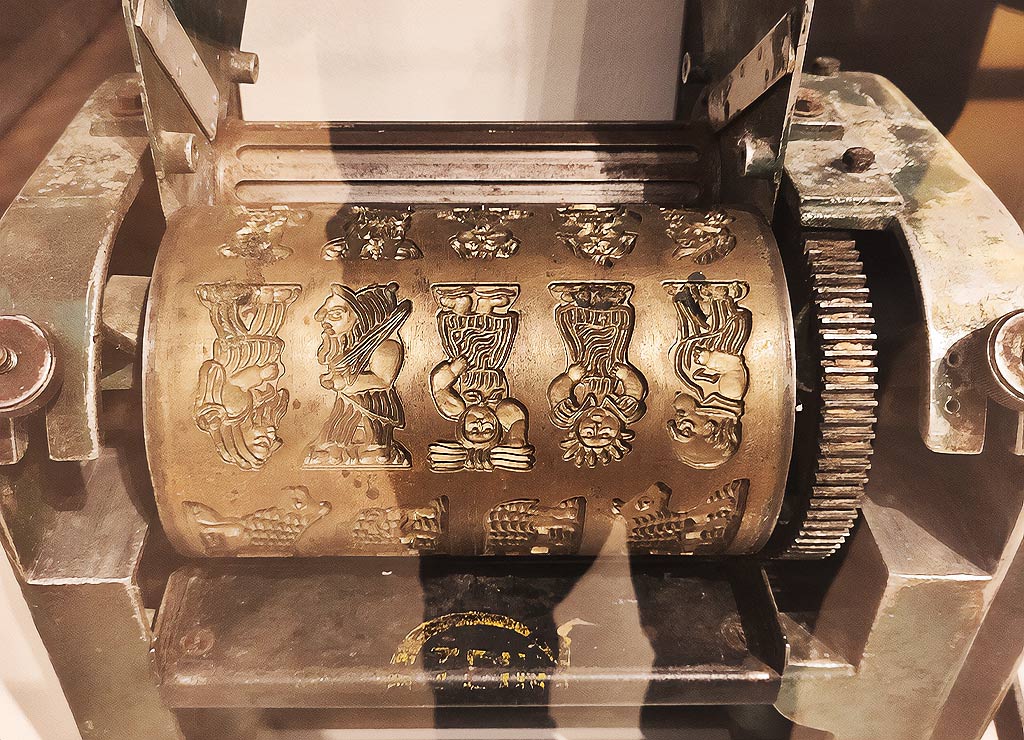 Eine antike Spekulatiusmaschine mit typischen Figuren auf einer Walze. Tag der Spekulatius in Deutschland. Kuriose Feiertage - 2. Dezember © 2023 Sven Giese – Bild 4 Eine antike Spekulatiusmaschine mit typischen Figuren auf einer Walze aus Metall, aufgenommen in einer Nahaufnahme.