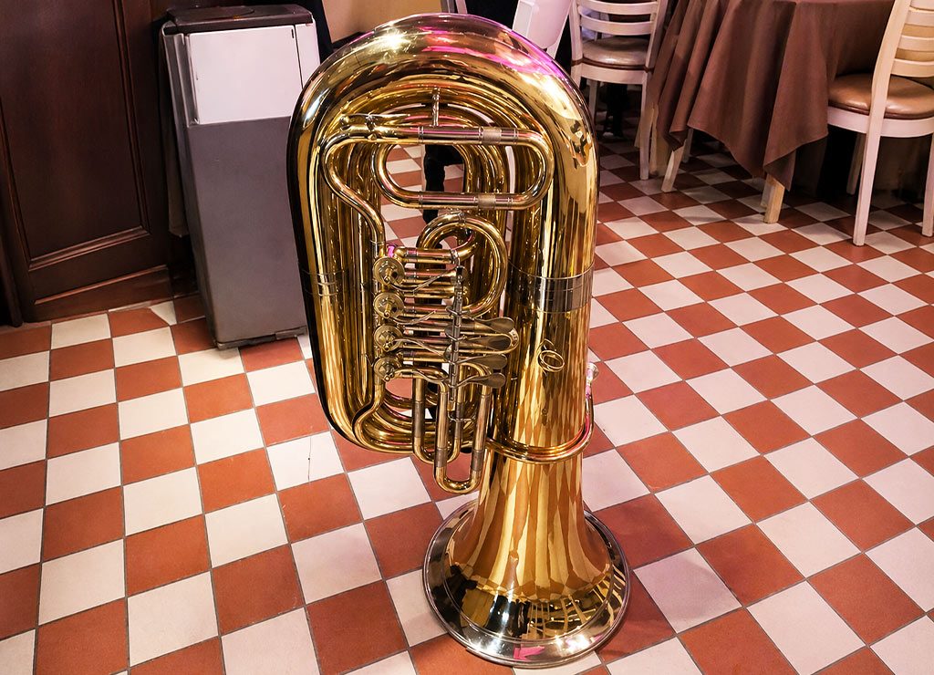 Goldglänzende Tuba steht auf kariertem Fliesenboden in einem Restaurant oder Saal.