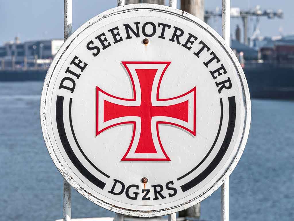 Tag der Seenotretter in Deutschland. Kuriose Feiertage – letzter Sonntag im Juli © 2025 Sven Giese – Bild 3 Rundes DGzRS-Schild mit rotem Kreuz und Schrift „Die Seenotretter“.