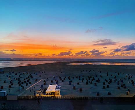 Bunter Sonnenuntergang über einem Nordseestrand mit vielen leeren Strandkörben.
