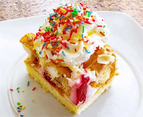 Stück Eiswaffelkuchen mit Sahnehaube und bunten Streuseln auf weißem Teller.