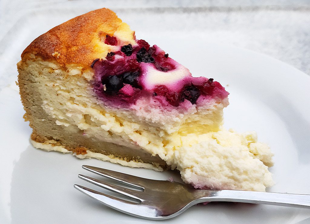 Ein Stück Cranberry-Käsekuchen auf einem weißen Teller, garniert mit roten Beeren.
