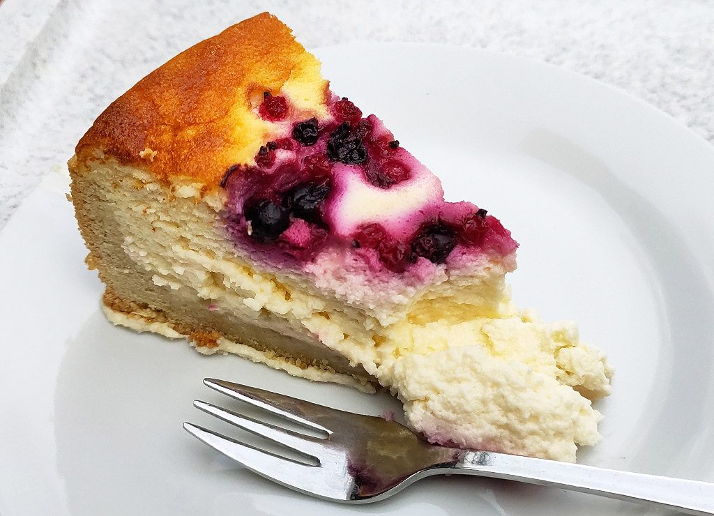 Ein Stück Cranberry-Käsekuchen auf einem weißen Teller mit Kuchengabel.