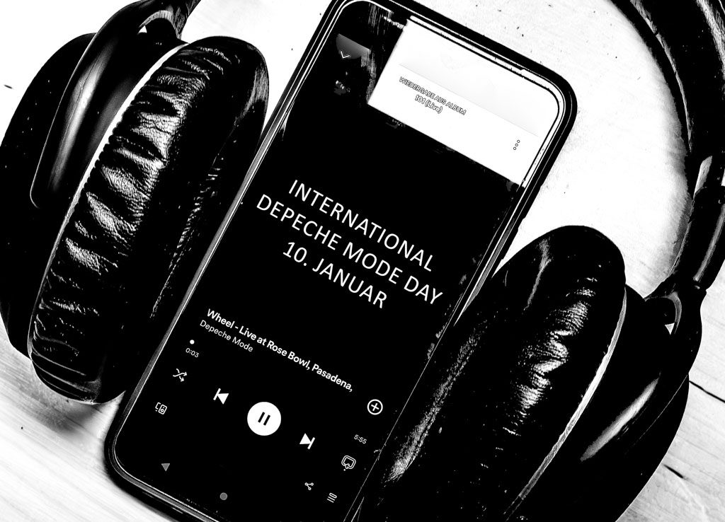 Smartphone mit Kopfhörern, zeigt den Text "International Depeche Mode Day 10. Januar".